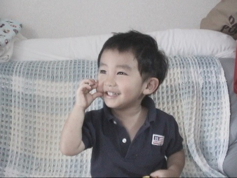 小さな男の子が人差し指と親指でほっぺをつまんで笑顔